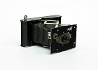 img 0003  Aparat produkowany w latach 1915 – 1926. Film zwojowy o szerokości 4 cm. Przesłona 1, 2, 3, 4 – opisana jako motywy: portret, średni, odległy obiekt. Czasy B, T 1/25 – 1/50 s. Odległość hiperfokalna . Miech w kolorze czarnym. Aparat w tylnej ściance posiadał podłużną otwieraną klapkę, po otwarciu której na boku zdjęcia można było wykonywać specjalnym rysikiem napisy.