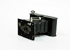 img 0004  Aparat produkowany w latach 1915 – 1926. Film zwojowy o szerokości 4 cm. Przesłona 1, 2, 3, 4 – opisana jako motywy: portret, średni, odległy obiekt. Czasy B, T 1/25 – 1/50 s. Odległość hiperfokalna . Miech w kolorze czarnym. Aparat w tylnej ściance posiadał podłużną otwieraną klapkę, po otwarciu której na boku zdjęcia można było wykonywać specjalnym rysikiem napisy.
